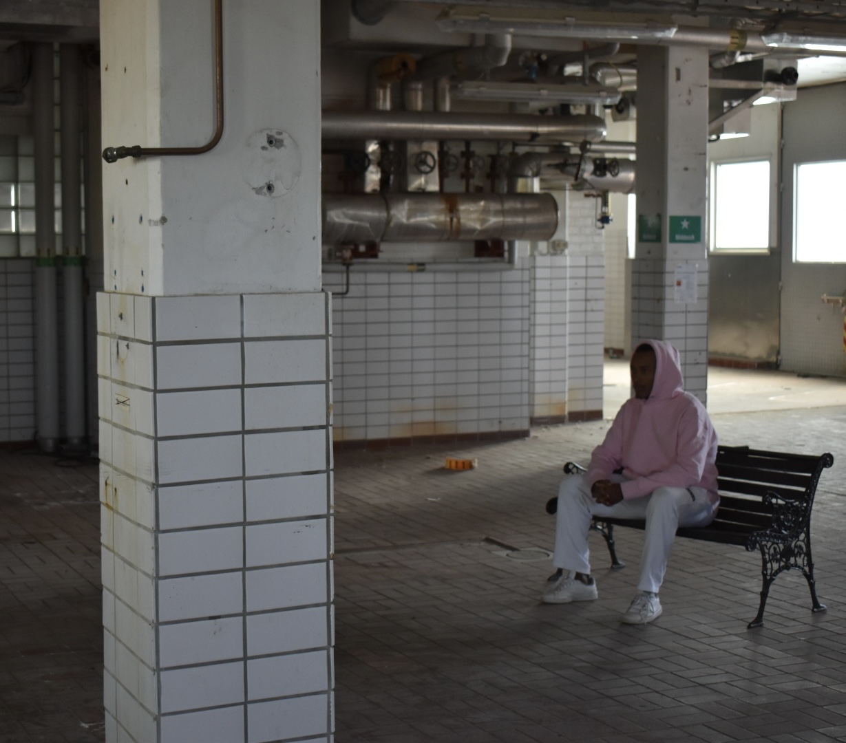 Emil seated in an industrial hall wearing a pink hoodie